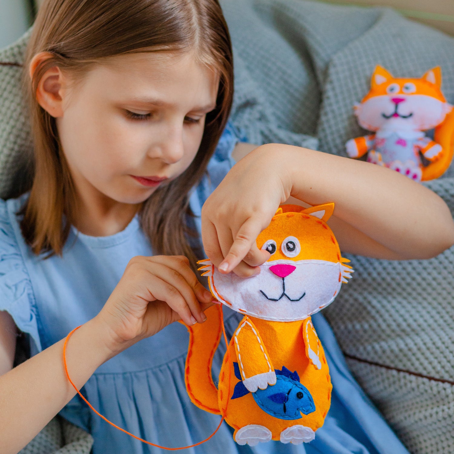 Flicka syr ett filtdjur som är en orange katt med en blå fisk i handen.