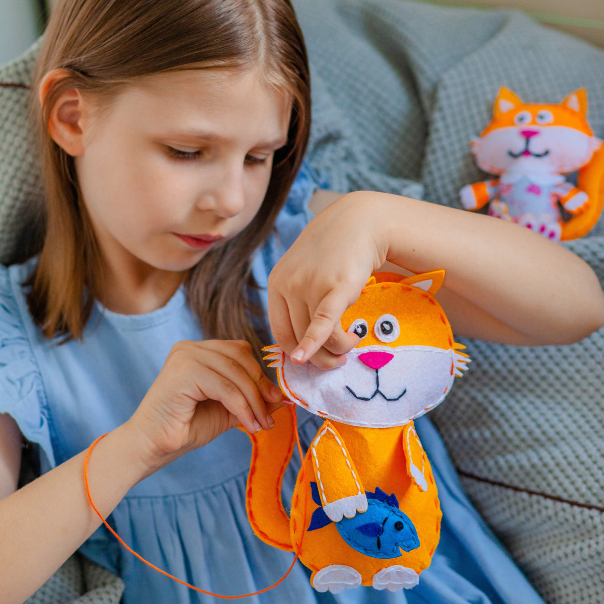 Flicka syr ett filtdjur som är en orange katt med en blå fisk i handen.