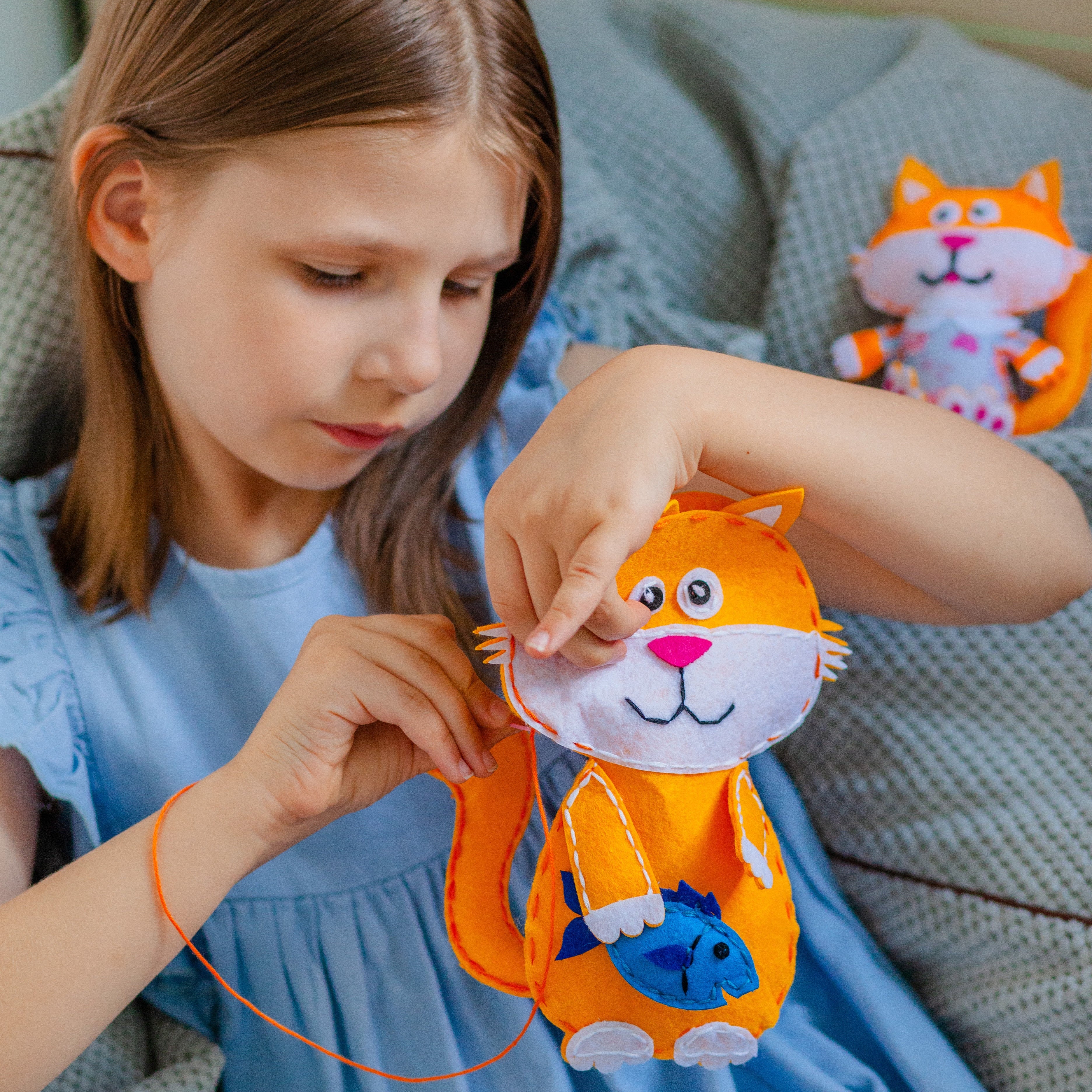 Flicka syr ett filtdjur som är en orange katt med en blå fisk i handen.